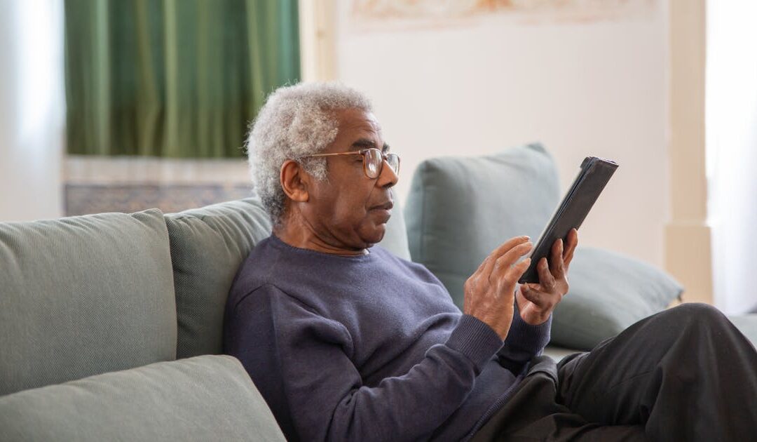 Senior man reading on tablet while receiving home care in Toronto